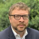 Professional close up headshot of a man in a suit and glasses.