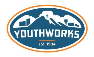 Oval-shaped logo with white text reading "Youthworks est. 1994" amidst a silhouette of skyscrapers and a mountain.