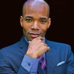 Headshot of a man in a suit resting his hand on his chin thoughtfully.