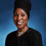 Headshot of a woman smiling at the camera and posing in front of a plain blue background.