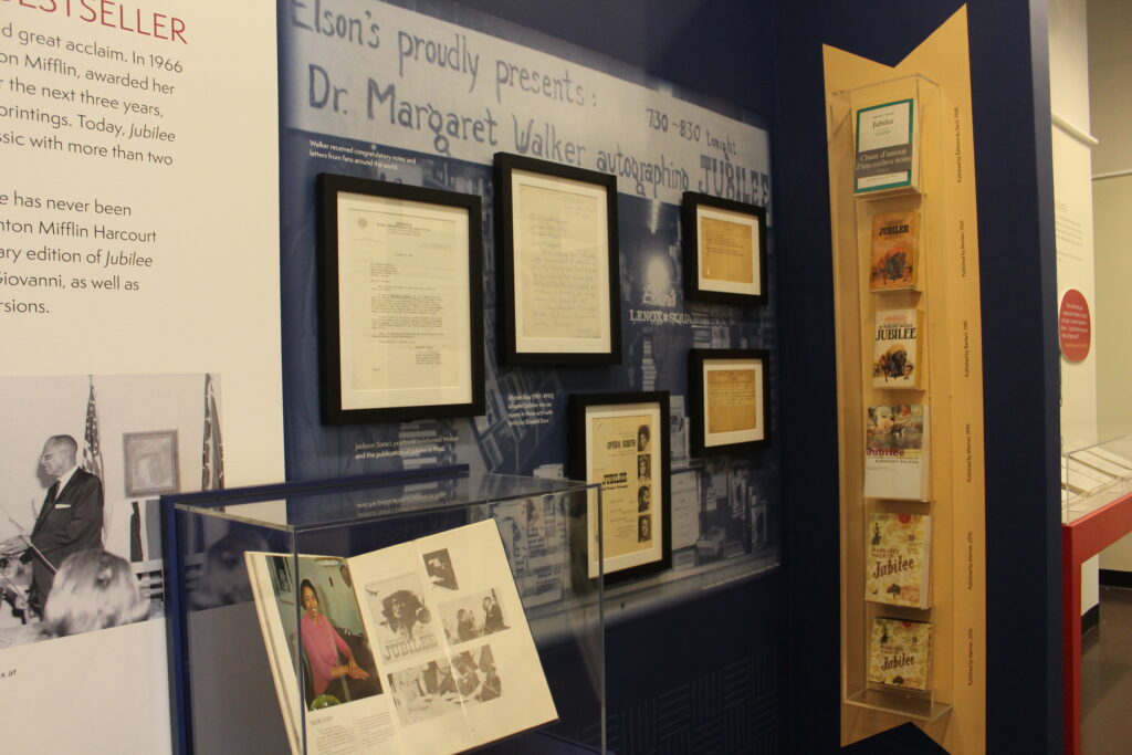 An exhibit wall displays blocks of text, photos, framed documents, and a column of different copies of Margaret Walker's novel Jubilee.